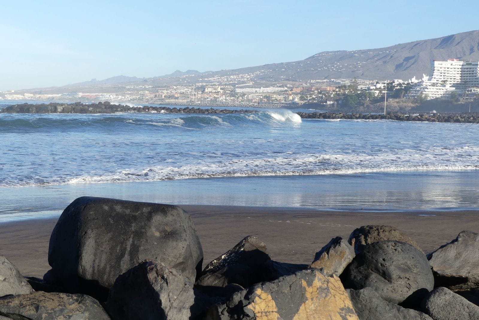 Waves breaking towards a dark sand beach at Playa de las Américas, December 2018.